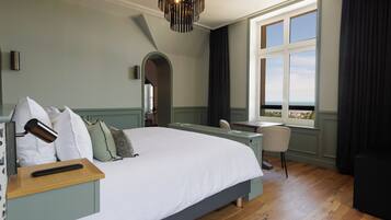 Een slaapkamer met een groot bed, een bureau en een stoel. Er is een raam met uitzicht op het omliggende landschap.