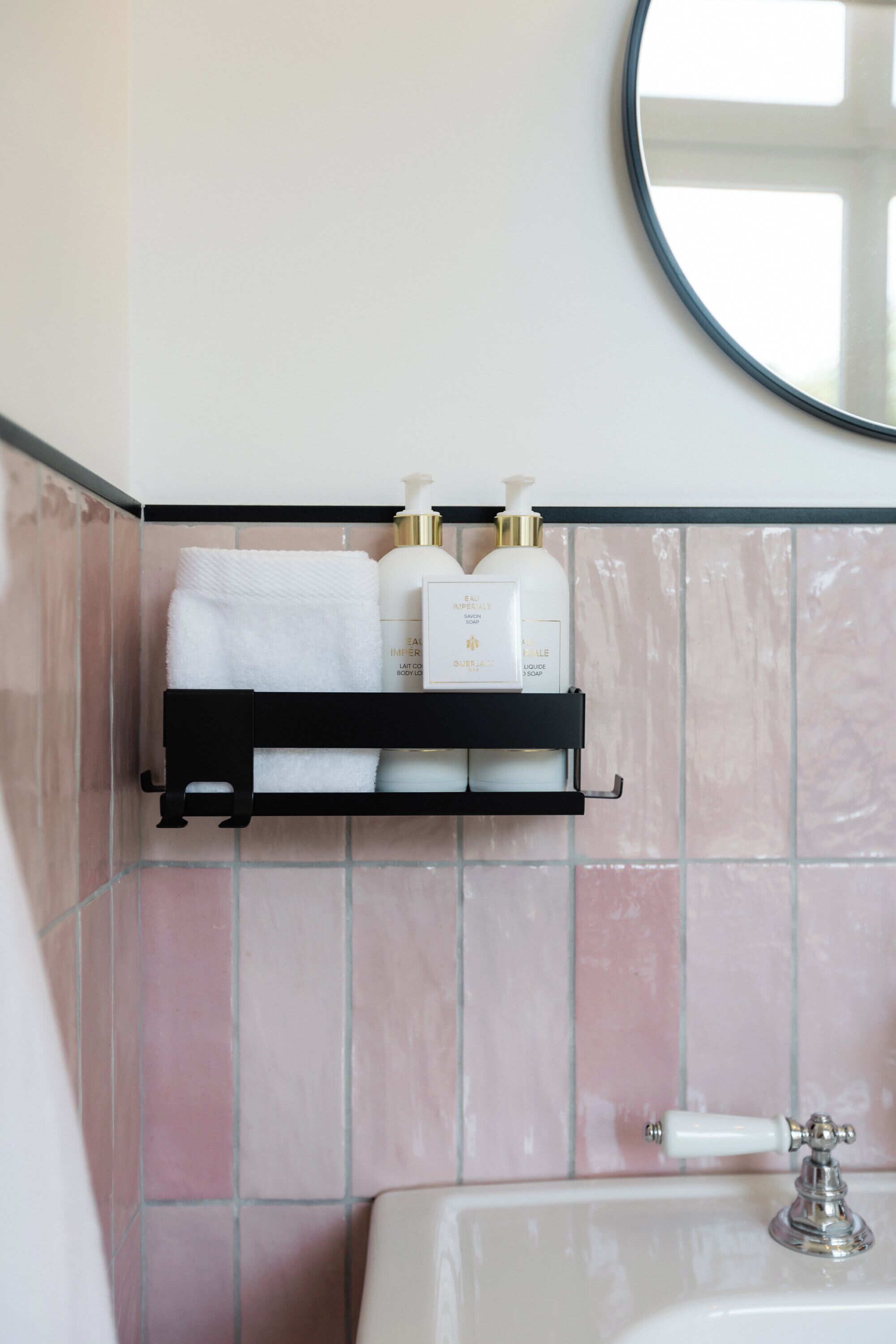 A bathroom with a white sink, a mirror above it, and a black shelf holding toiletries and a white towel.