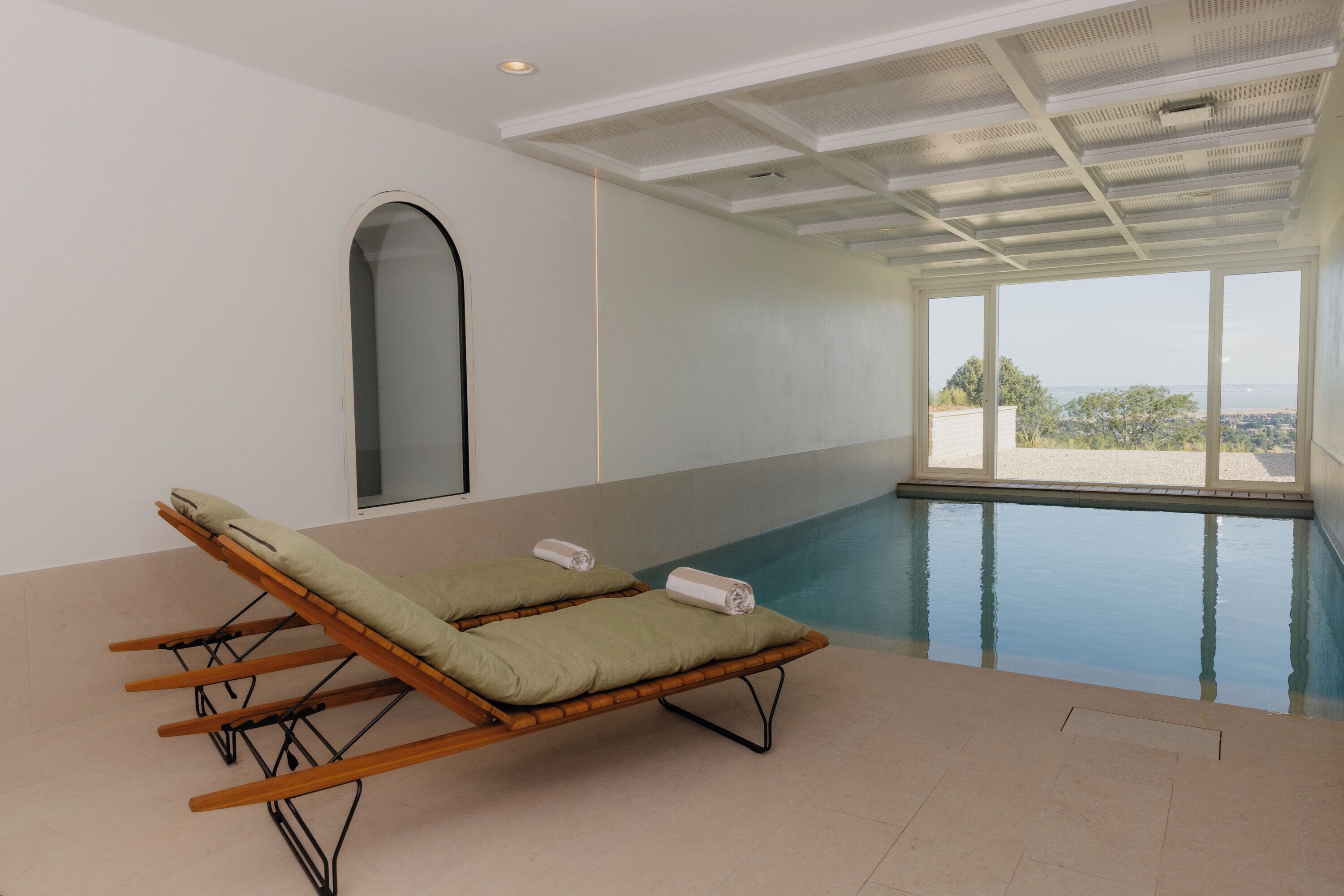 Ein Poolbereich mit zwei Liegestühlen und einem großen Fenster mit Blick auf eine Landschaft.
