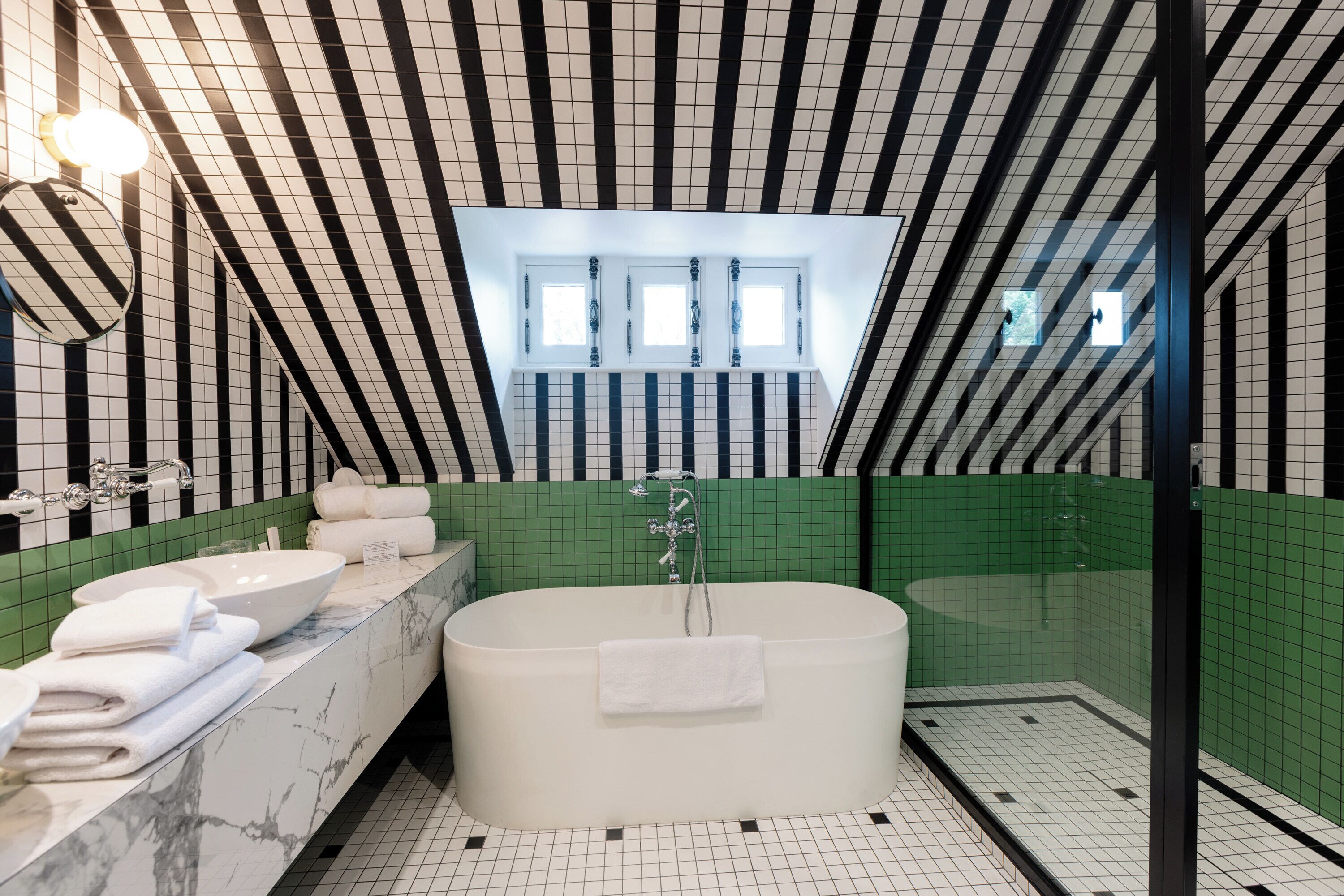 A modern bathroom with a freestanding bathtub, a vanity with a marble countertop, and a green-tiled shower area.