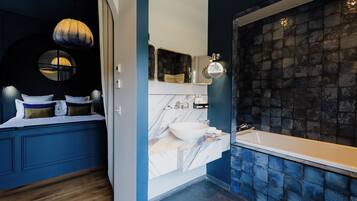Une salle de bain moderne avec un grand miroir, une fenêtre ronde et une baignoire dont le mur est recouvert de carreaux.