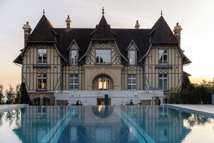 Um edifício grande e histórico com fachada simétrica, entrada central e piscina ao redor.