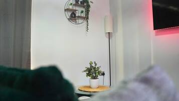 A room with a white wall, a round shelf with plants, a lamp, and a TV.
