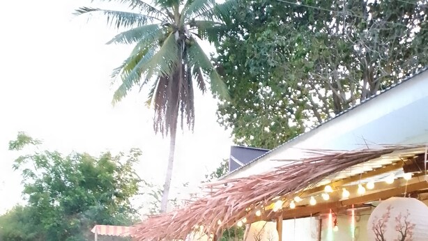 An outdoor dining area with a thatched roof, wooden stools, and a bar counter. - 8hotel (Bantayan)