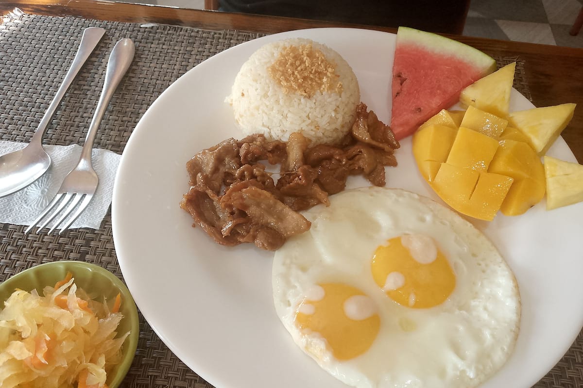 A plate with rice, meat, eggs, and fruit.