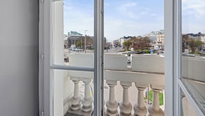 Uitzicht vanaf een balkon met balustrade, op een straat met gebouwen en geparkeerde auto's.
