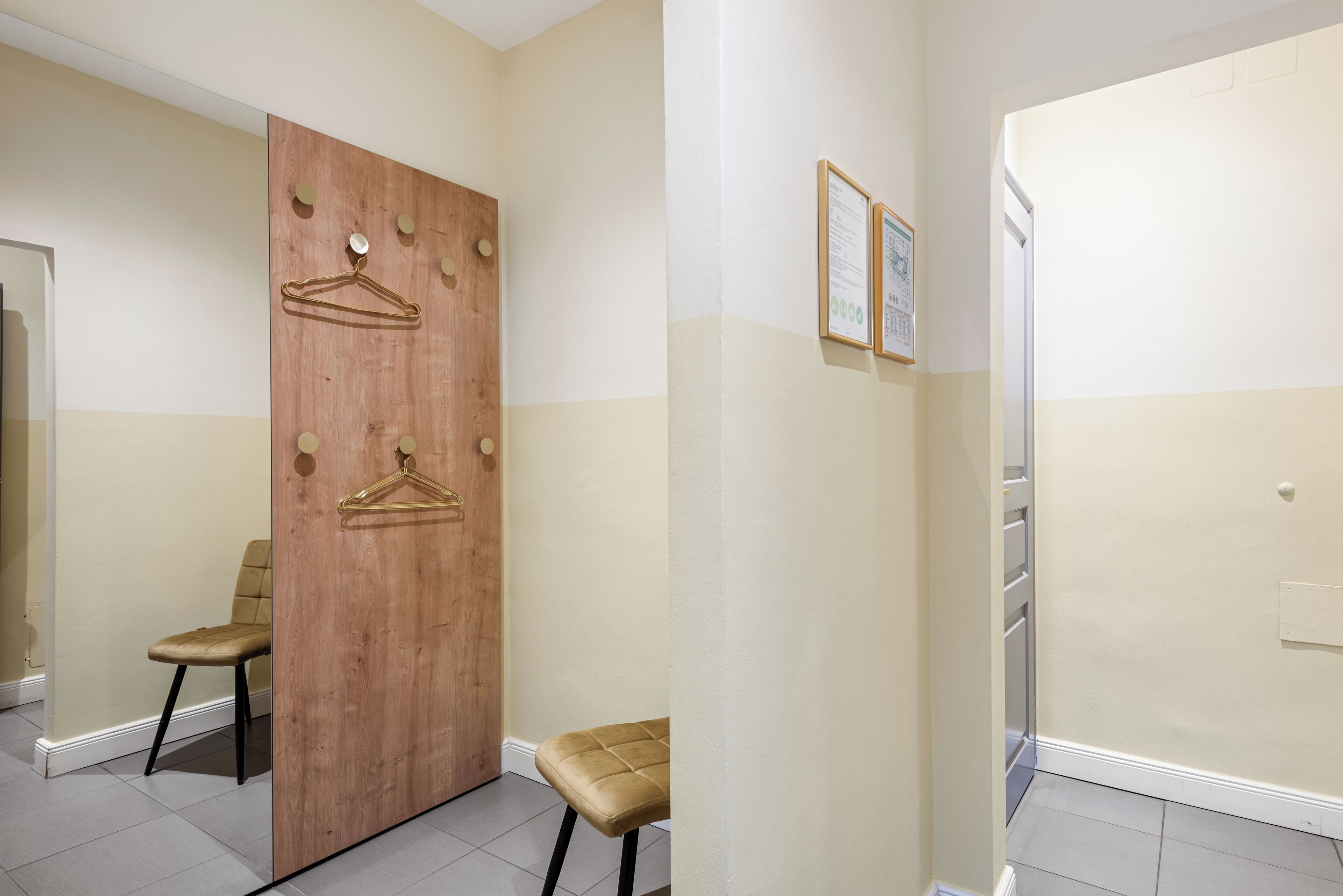 Un pasillo con una puerta de madera, dos sillas y un cartel enmarcado en la pared.