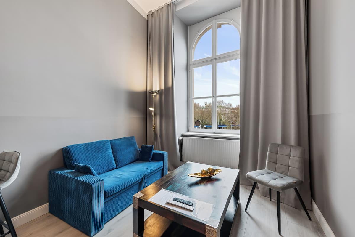 A modern living room with a blue sofa, a wooden coffee table with a remote control, and a grey armchair.
