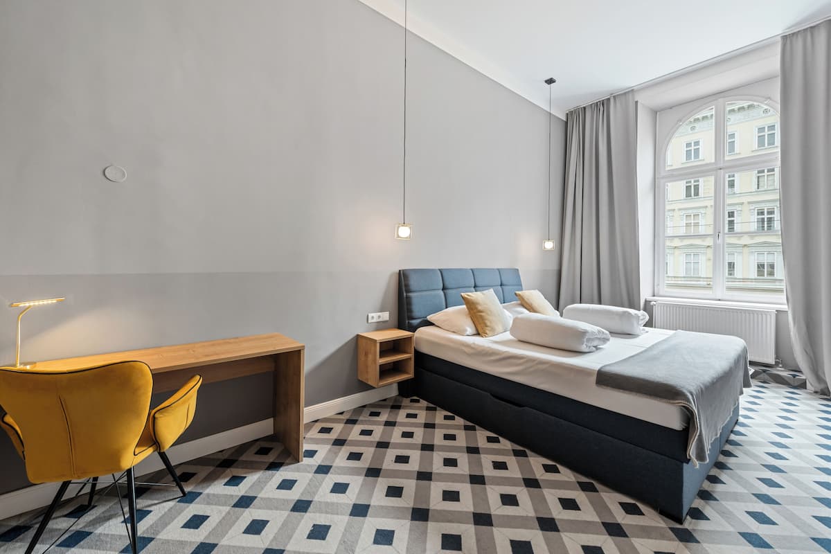 A modern hotel room with a bed, a desk, a chair, and a large window with curtains.