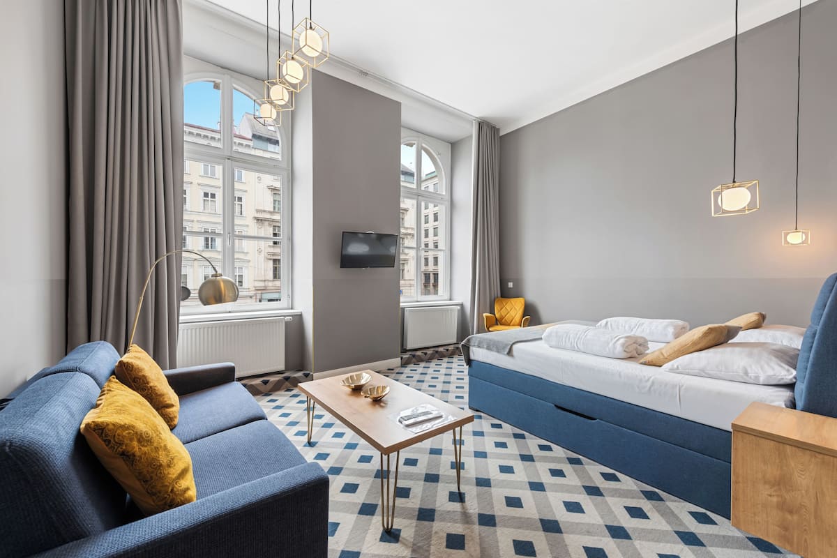 A modern hotel room with a sofa, a bed, a coffee table, and a TV.