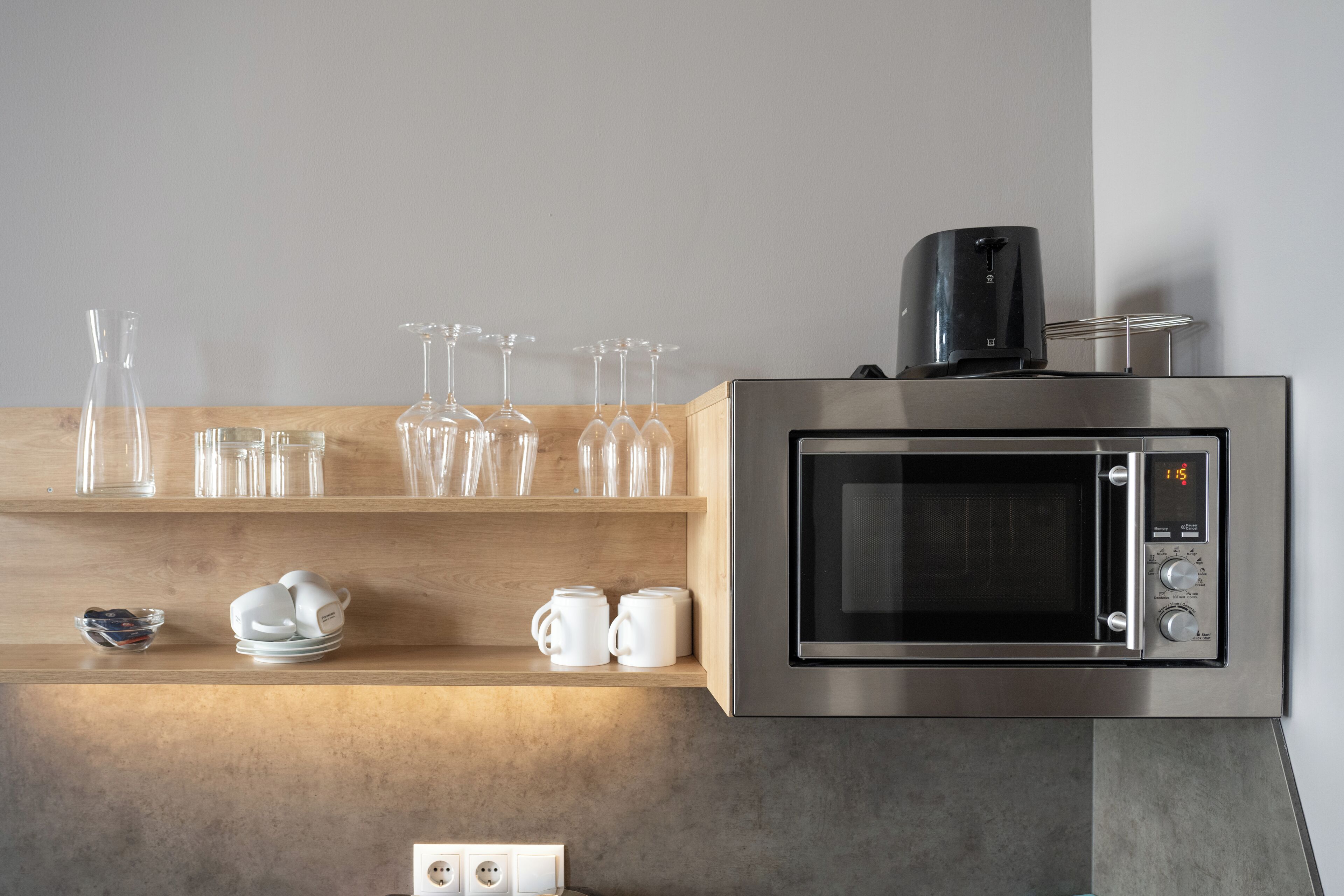 A kitchen with a stainless steel microwave, a coffee maker, and various glassware on shelves.
