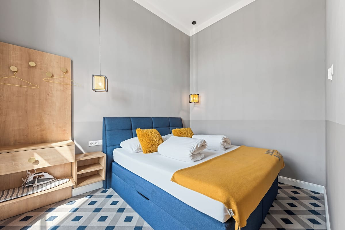 A modern bedroom with a blue bed, wooden wardrobe, and a geometric patterned floor.