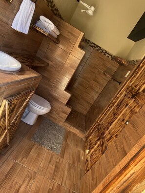 Une salle de bain moderne avec un plancher en bois, des toilettes blanches, un lavabo avec un miroir et un espace douche.