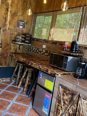 Une cuisine rustique aux murs et au plan de travail en bois. On y trouve un réfrigérateur, une machine à café et une bouilloire.