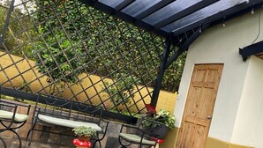 Ein Sitzbereich im Freien mit Stühlen und Pflanzenkübeln, eine Holztür und eine gelbe Wand.