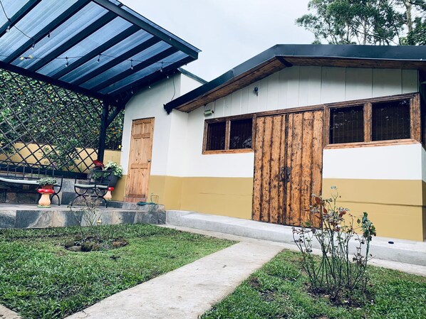 Une maison avec un patio couvert, une porte en bois et un petit jardin.