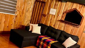 A cozy cabin-style room with a black sectional sofa, a colorful blanket, and a wooden interior. - The perfect escape to reconnect with nature and yourself.  (Alajuela)