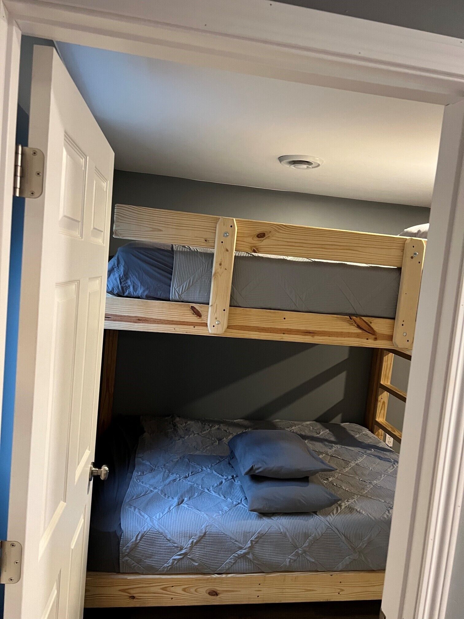 A bunk bed room with a door partially open, revealing a lower bunk with a mattress and pillows.