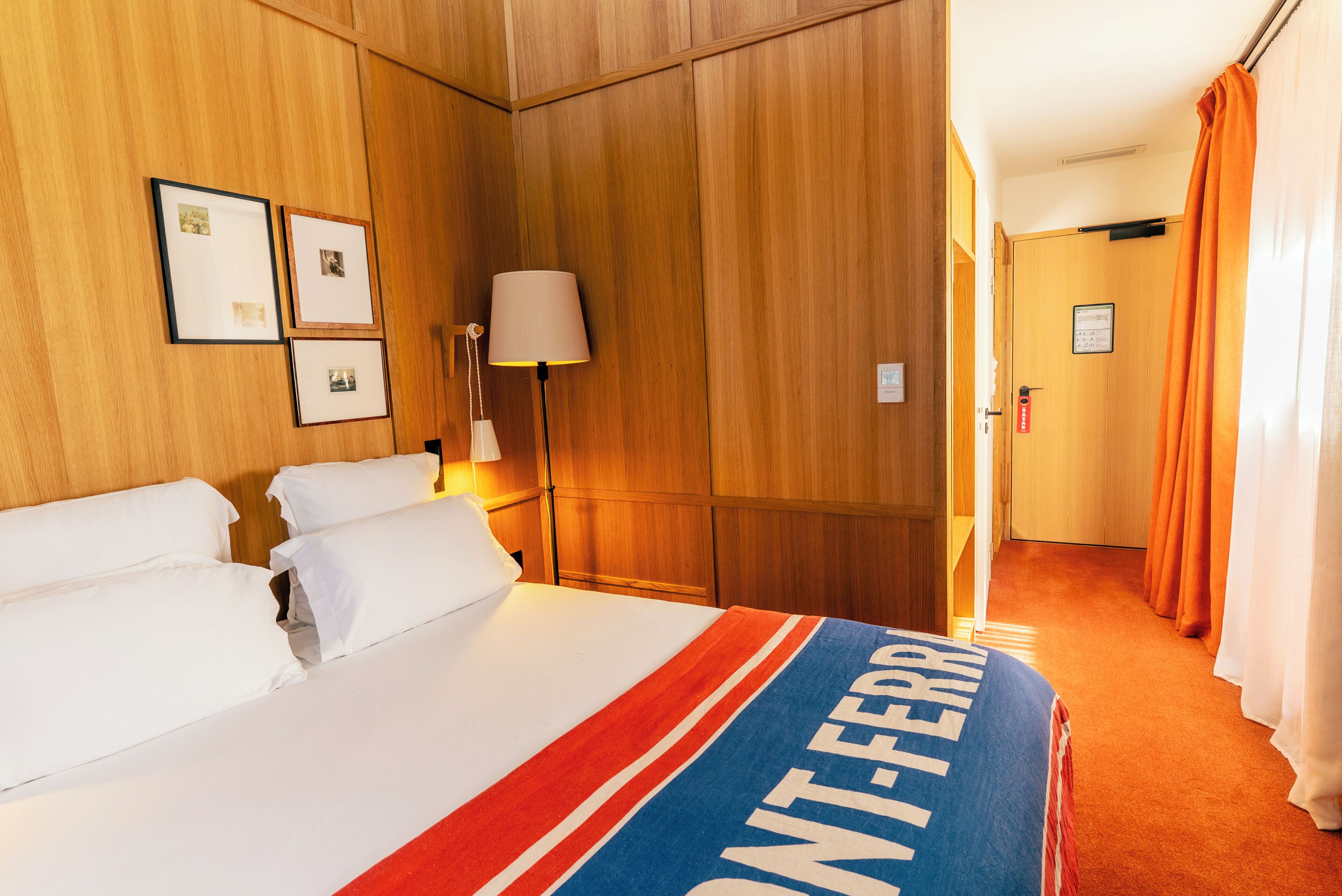 Ein Hotelzimmer mit Bett, Nachttisch, Lampe und einer Tür mit einem Schild.