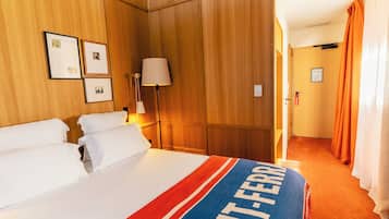 A hotel room with a bed, a nightstand, a lamp, and a door with a sign.