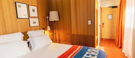 Ein Hotelzimmer mit Bett, Nachttisch, Lampe und einer Tür mit einem Schild.