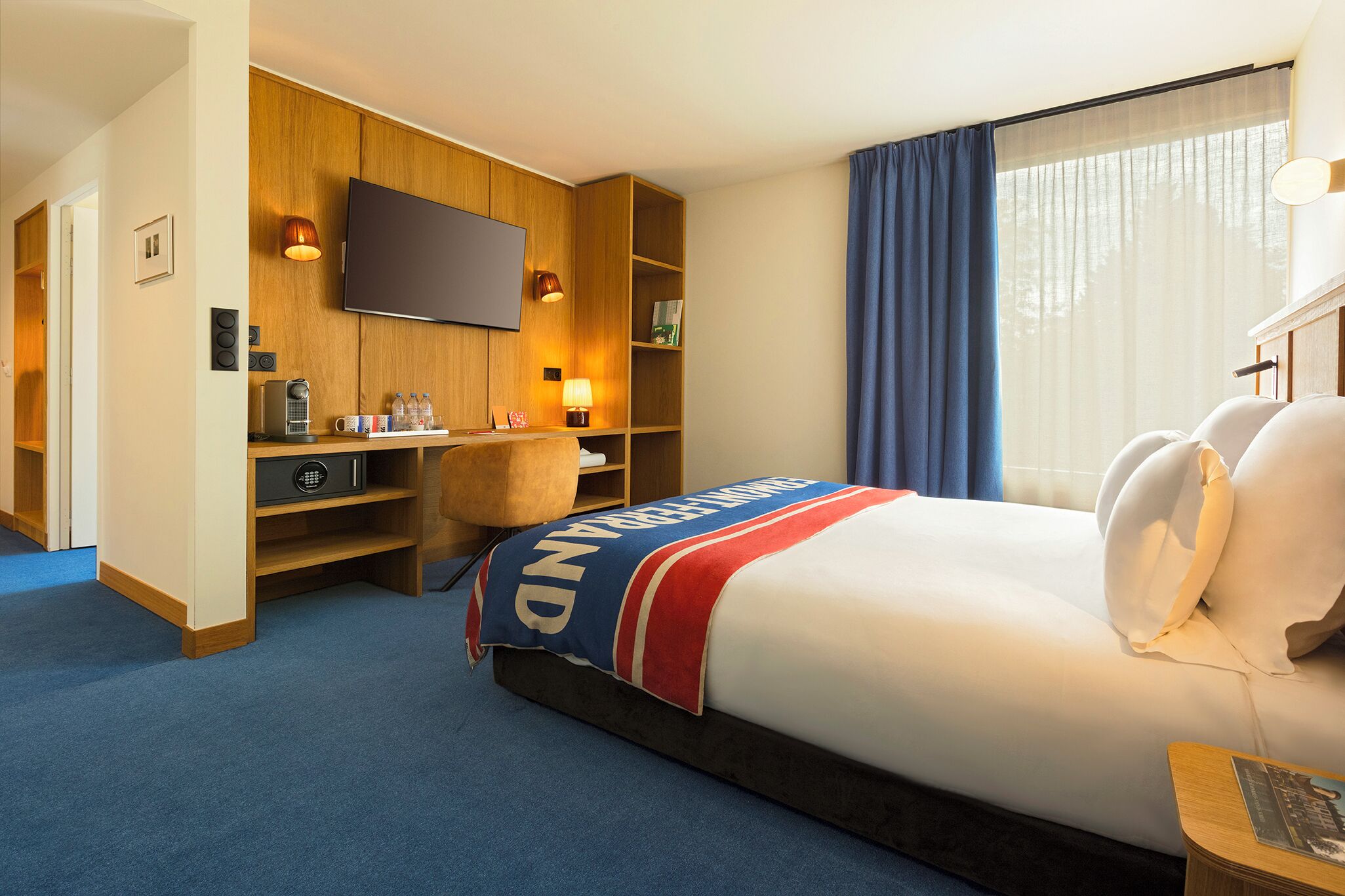 A hotel room with a bed, a desk, a television, and a window with curtains.