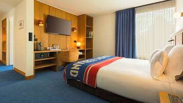 A hotel room with a bed, a desk, a television, and a window with curtains.