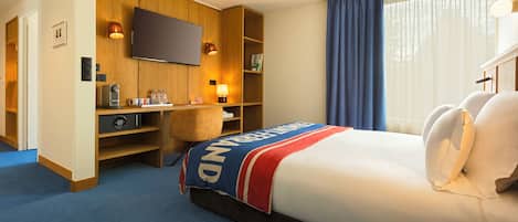 Una habitación de hotel con cama, escritorio, televisor y ventana con cortinas.