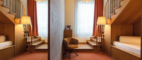 A hotel room with a bed, a chair, a desk, a mirror, and a staircase.