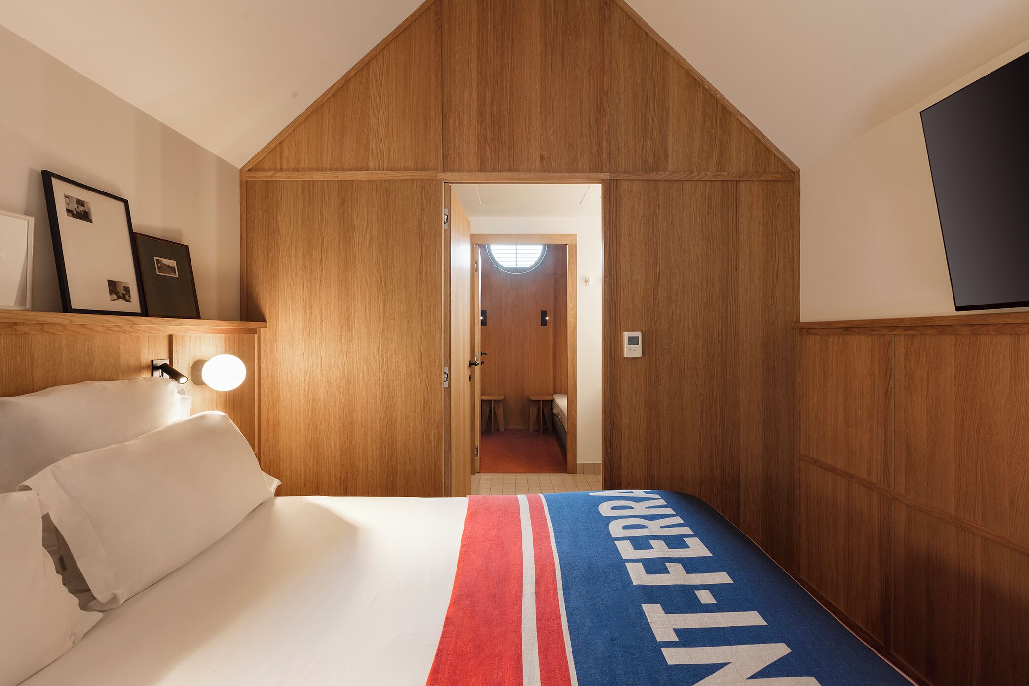 Una habitación de hotel con cama, mesita de noche, lámpara de pared, un cuadro y un armario de madera.