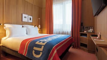 A hotel room with a bed, a desk, a television, and a window with curtains.