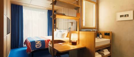 A hotel room with a bed, a desk, a mirror, a sink, and a shower area.