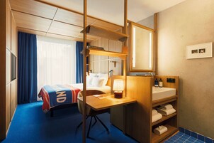 Una habitación de hotel con cama, escritorio, espejo, lavamanos y zona de ducha.