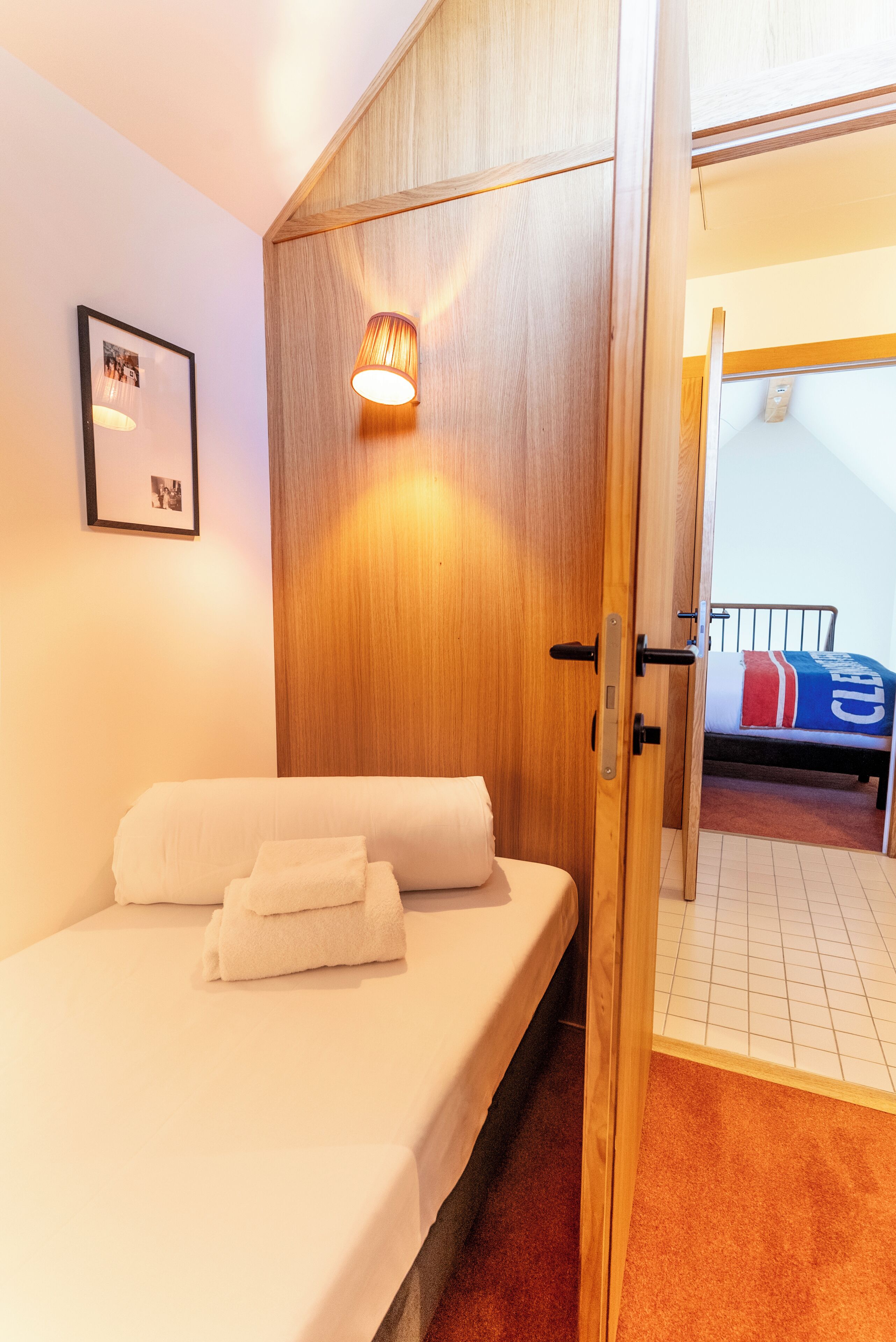 Un dormitorio con cama, armario de madera, un cuadro en la pared y un baño visible a través de una puerta abierta.