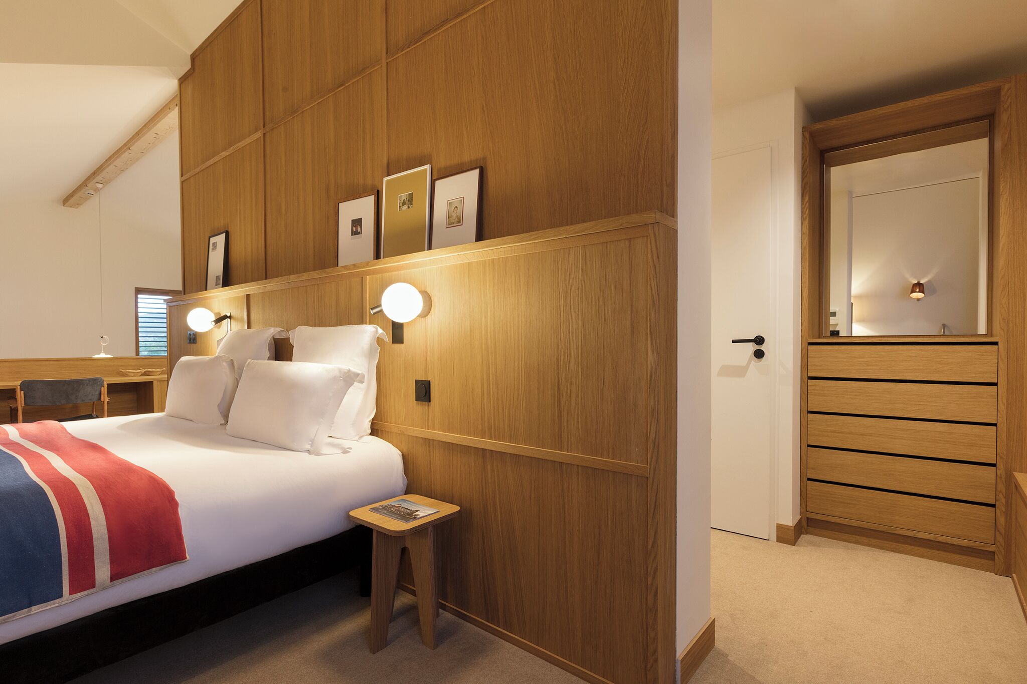 A bedroom with a bed, bedside table, wall-mounted lights, a mirror, and a wardrobe.