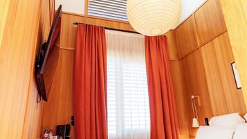 A bedroom with a bed, a desk, a hanging light fixture, and a window with curtains.