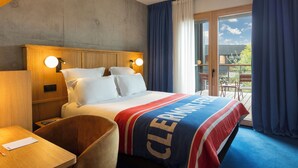 A hotel room with a bed, a wooden nightstand, a desk, and a chair. There is a balcony with a view of the sky and trees. - GRAND MESS Clermont-Ferrand (Clermont-Ferrand)