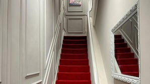 A grand staircase with red carpeted steps and a white wall with a framed picture. - Studio Flat in Ealing Broadway (London)