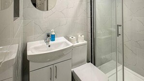 A bathroom with a white sink, mirror, toilet, and glass shower enclosure. - Studio Flat in Ealing Broadway (London)