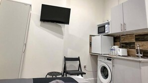 A compact bedroom with a bed, a washing machine, a microwave, and a small table with a chair. - Studio Flat in Ealing Broadway (London)