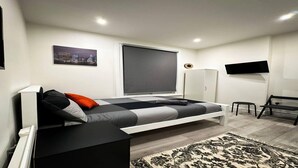 A modern bedroom with a bed, a TV, a wardrobe, and a cityscape painting. - Studio Flat in Ealing Broadway (London)