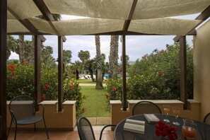 Zona de estar al aire libre techada, con vista a una piscina y palmeras.