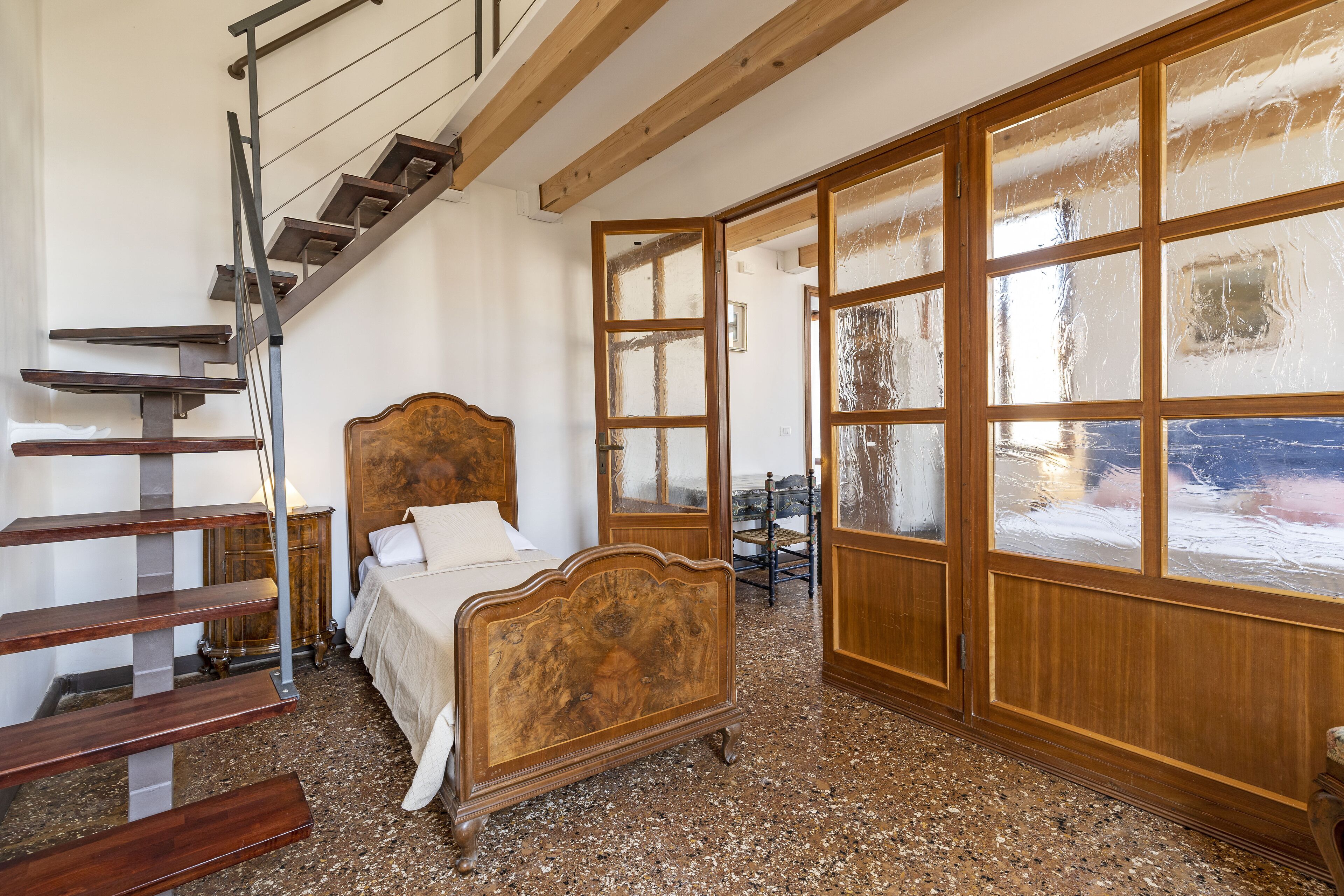 Een slaapkamer met een houten bed, een trap en een groot raam met geëtste glaspanelen.