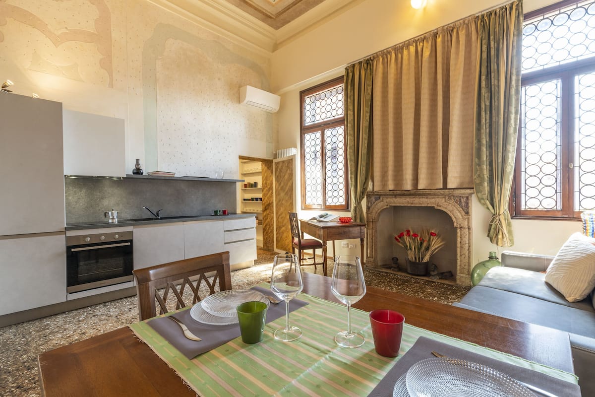 A cozy living room with a fireplace, a dining table with wine glasses, and a kitchen area with a stove and cabinets.