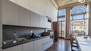 A modern kitchen with a large island, stainless steel appliances, and a view of the city through large windows. - Ca' Magia - Rialto Exclusive Residence by Wonderful Italy (Venice)