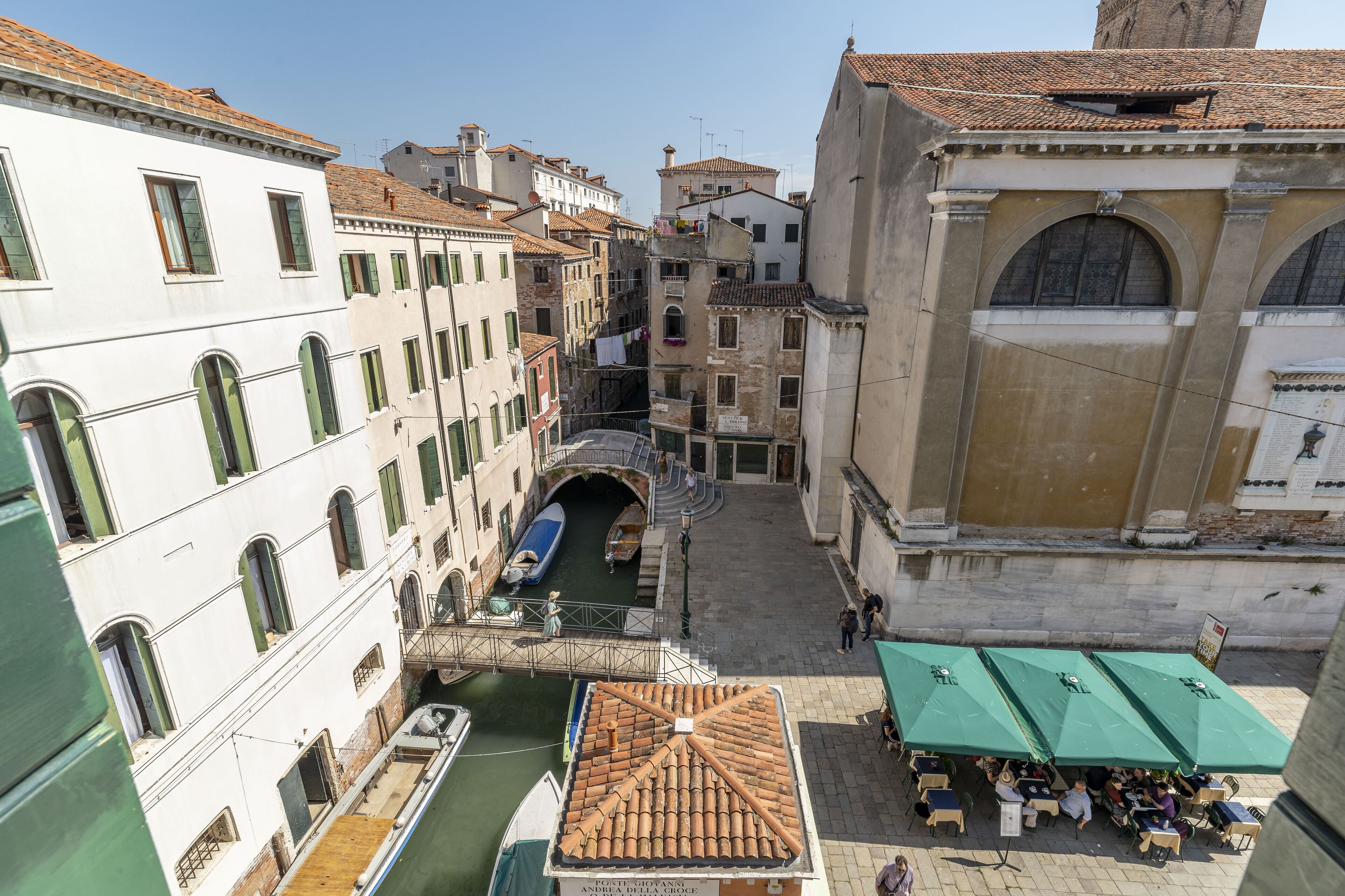 A narrow Venetian canal with buildings on either side, a bridge, and a boat docked at the canal's edge.