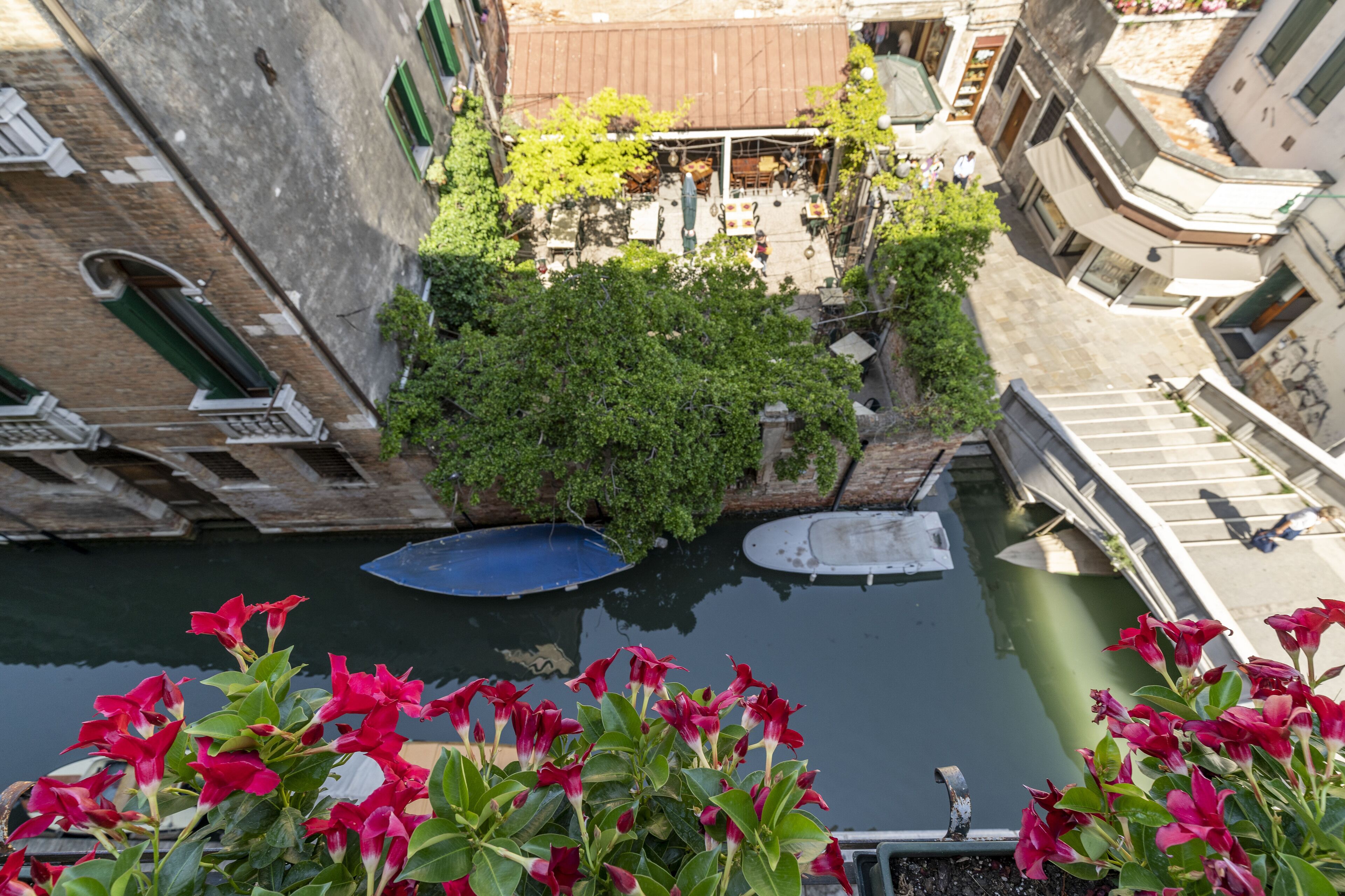 Un canal estrecho con barcos, rodeado de edificios con balcones y un pequeño jardín.