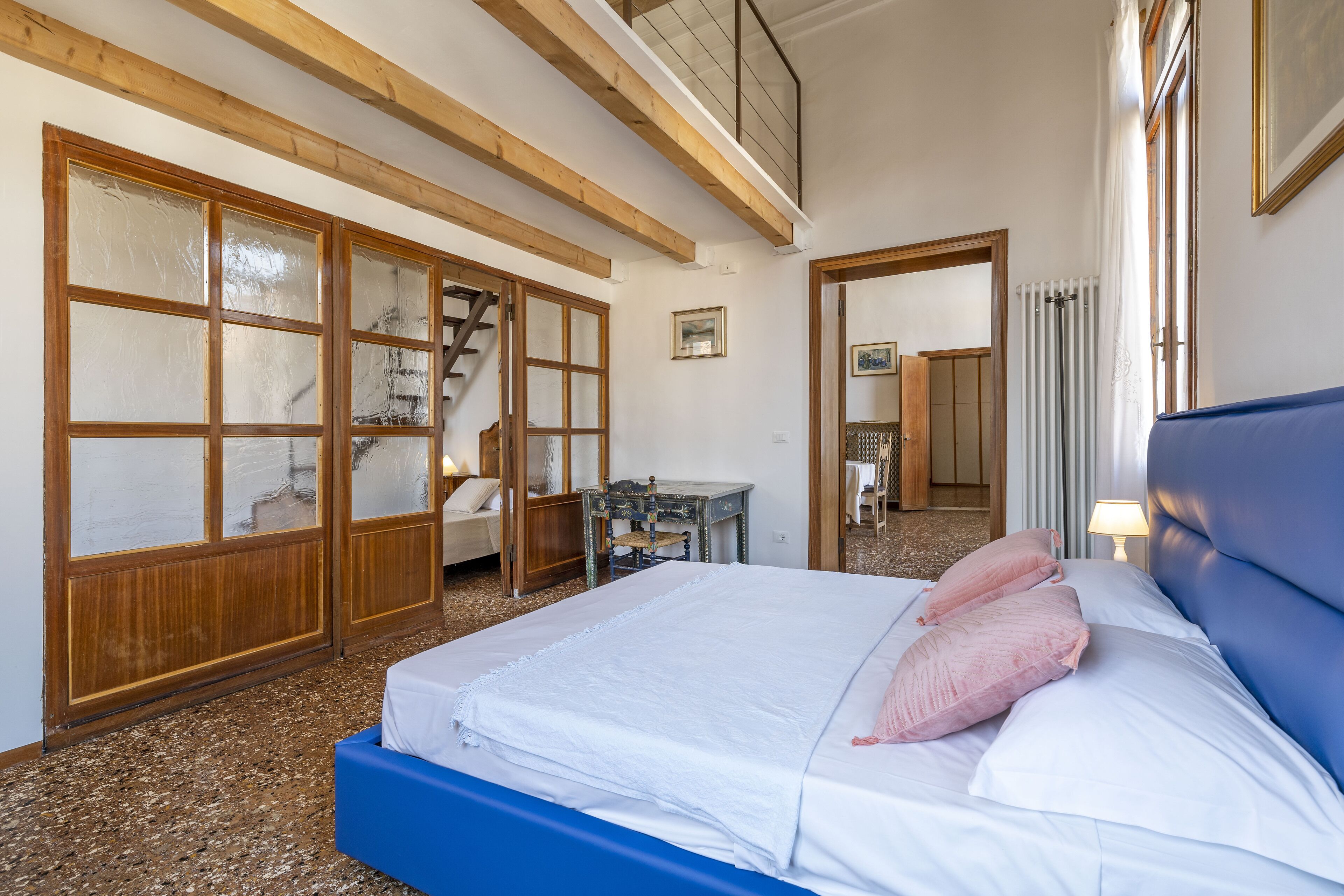Un dormitorio con una cama grande, vigas de techo de madera, un escritorio y una silla.