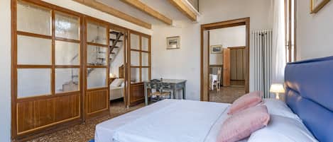 Un dormitorio con una cama grande, vigas de techo de madera, un escritorio y una silla.