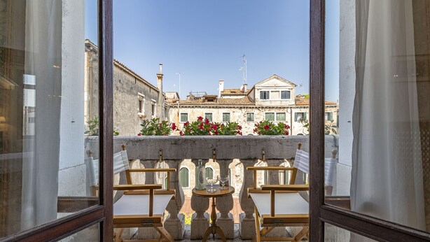 A balcony with a table and chairs, overlooking a building with a tiled roof and arched windows. - Ca' Magia - Rialto Exclusive Residence by Wonderful Italy (Venice)